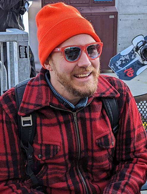 Spencer Kroll smiling in sunglasses, a red beanie, and a red and black flannel coat>
                        </div>

                        <div class=