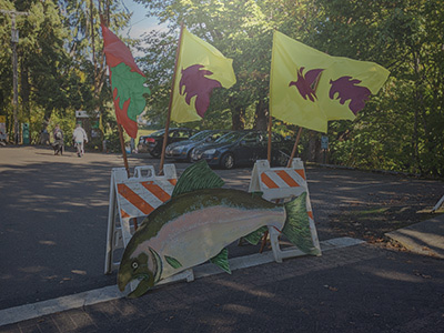 Road barricade with wooden salmon sign and fall themed flags attached.