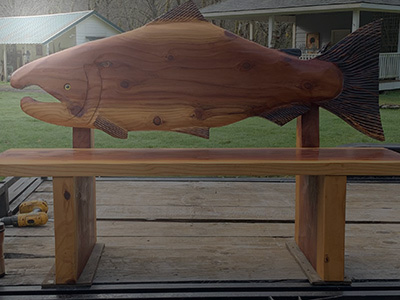 Wooden bench with carved wooden salmon for a back.